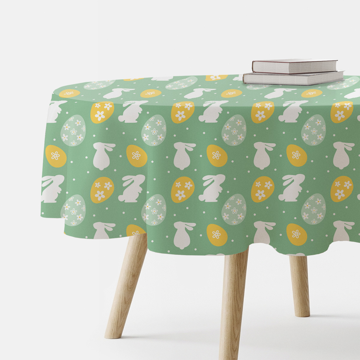 Okrągły obrus z motywem białych zajączków i żółtych pisanek na zielonym tle rozłożony na drewnianym stole
