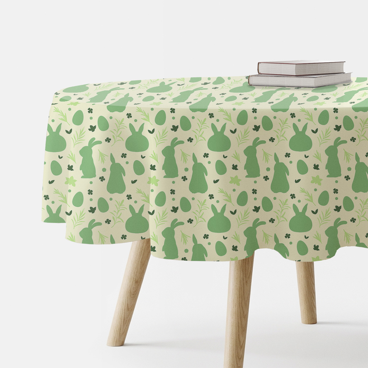 Okrągły obrus z zielonymi sylwetkami zajączków i pisanek na kremowym tle, widok boczny stołu z książkami