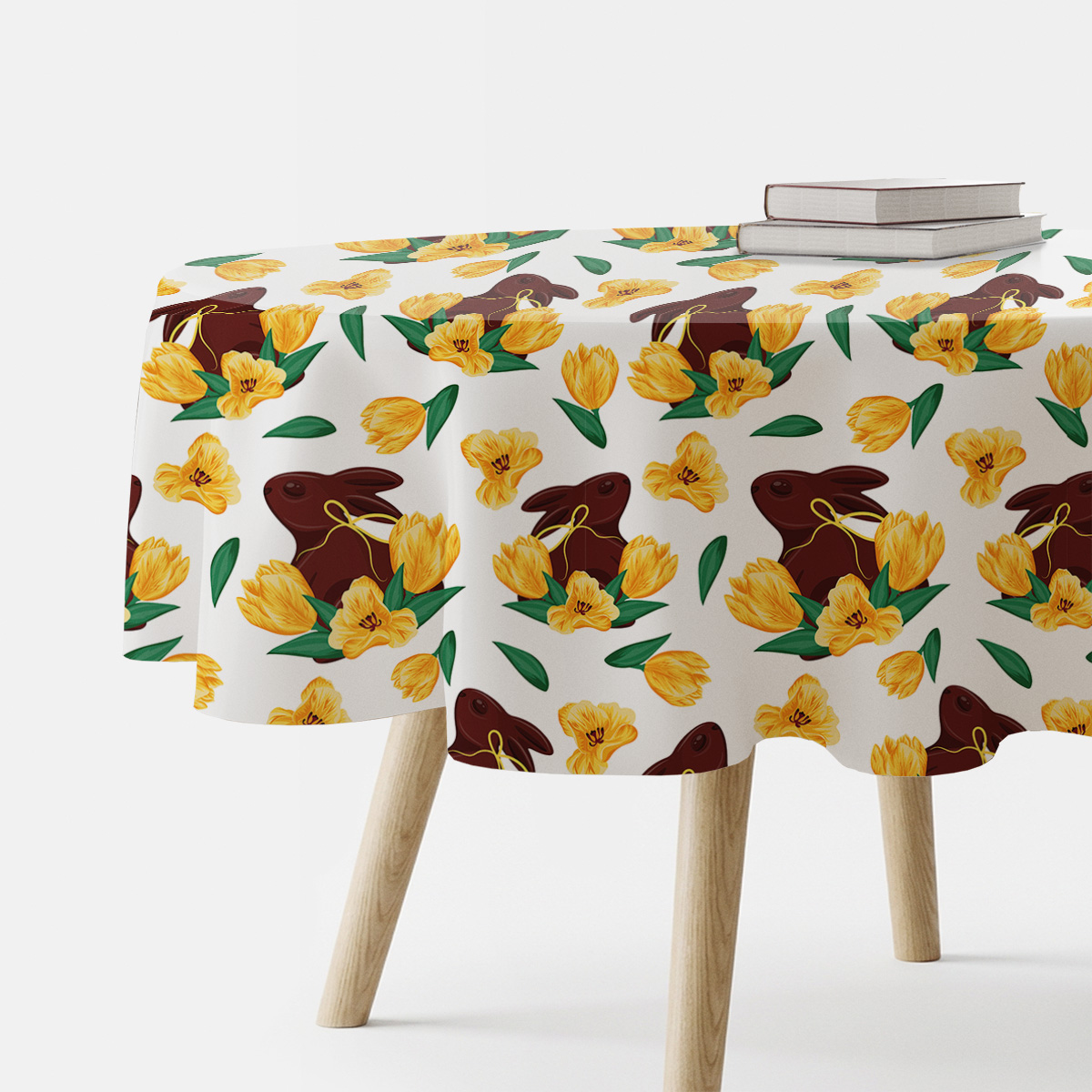 Okrągły obrus z motywem czekoladowych zajączków i żółtych tulipanów na jasnym tle, ujęcie stołu z książkami