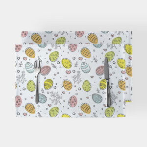 Dwie podkładki z motywem pastelowych pisanek i delikatnych gałązek ułożone na jasnym tle, widok z góry ze sztućcami