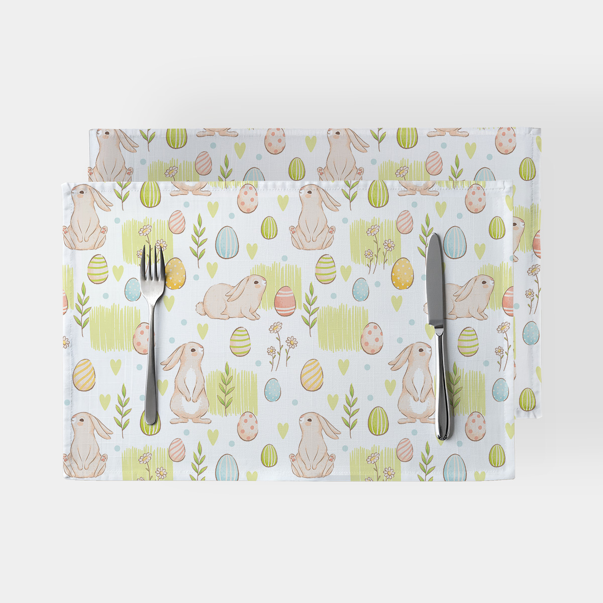 Para podkładek na stole z motywem króliczków i pisanek, widok z góry z leżącymi sztućcami