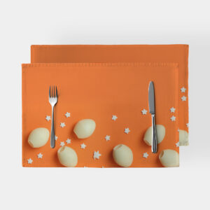 Pomarańczowa podkładka z kremowymi pisankami i białymi gwiazdkami, ujęcie produktowe ze sztućcami