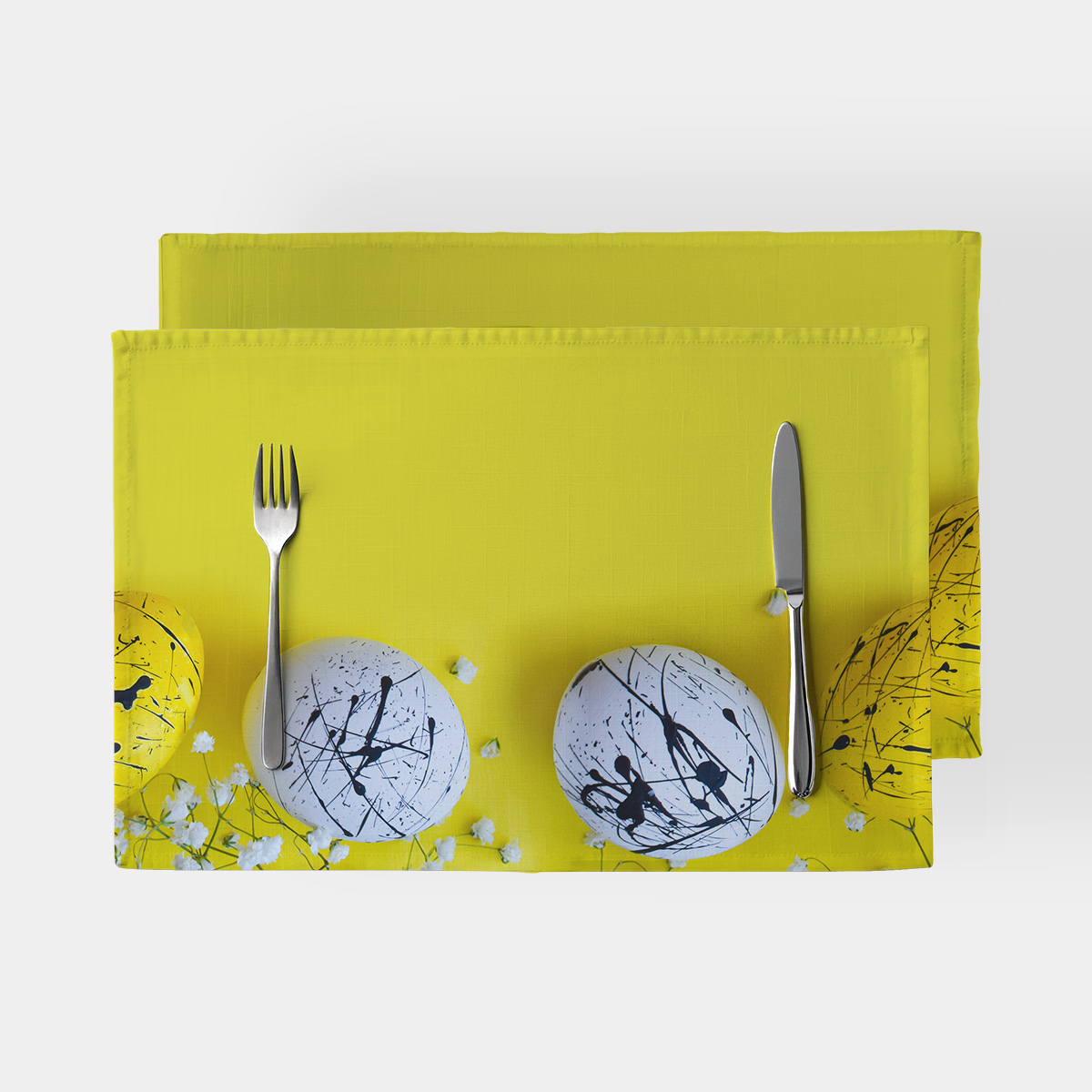 żółta podkładka z białymi pisankami ozdobionymi czarnymi, abstrakcyjnymi smugami widok z góry