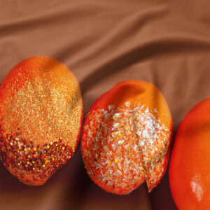 zbliżenie na pomarańczowe pisanki z brokatową i opalizującą fakturą na tkaninie