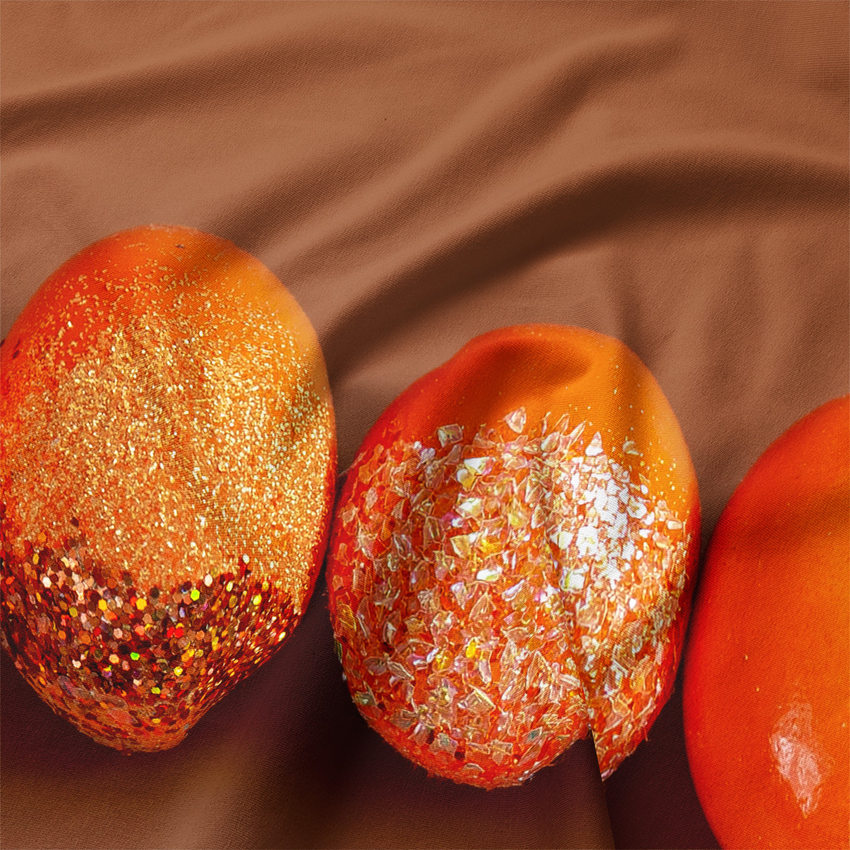 zbliżenie na pomarańczowe pisanki z brokatową i opalizującą fakturą na tkaninie
