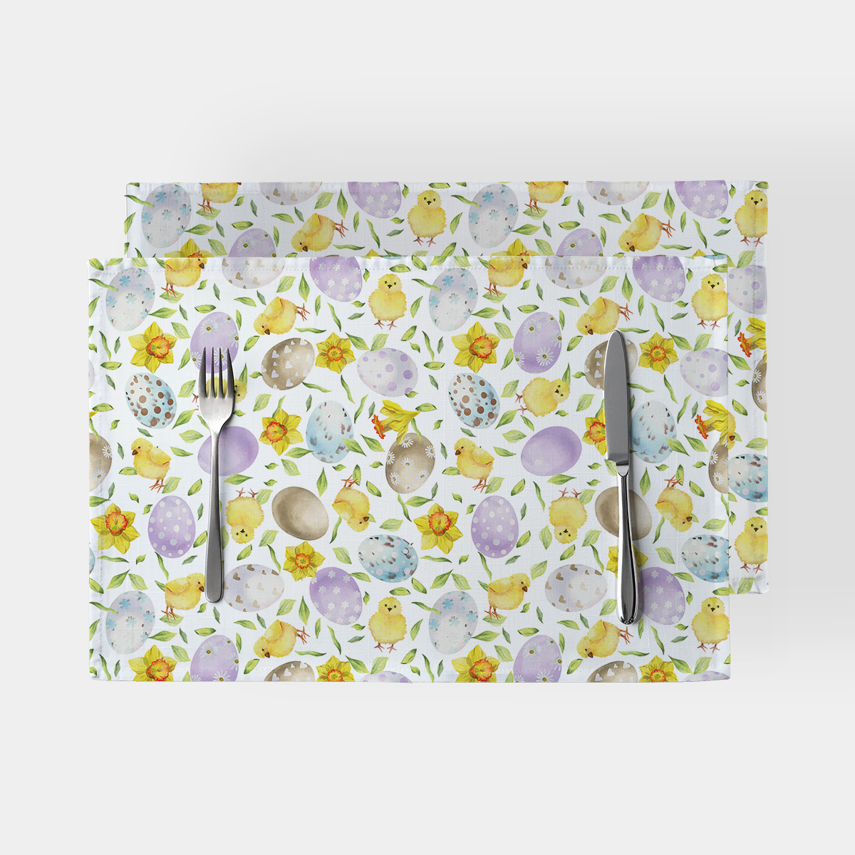 Podkładki na stół z wzorem akwarelowych pisanek i żółtych kurczaczków, widok z góry z ułożonymi sztućcami