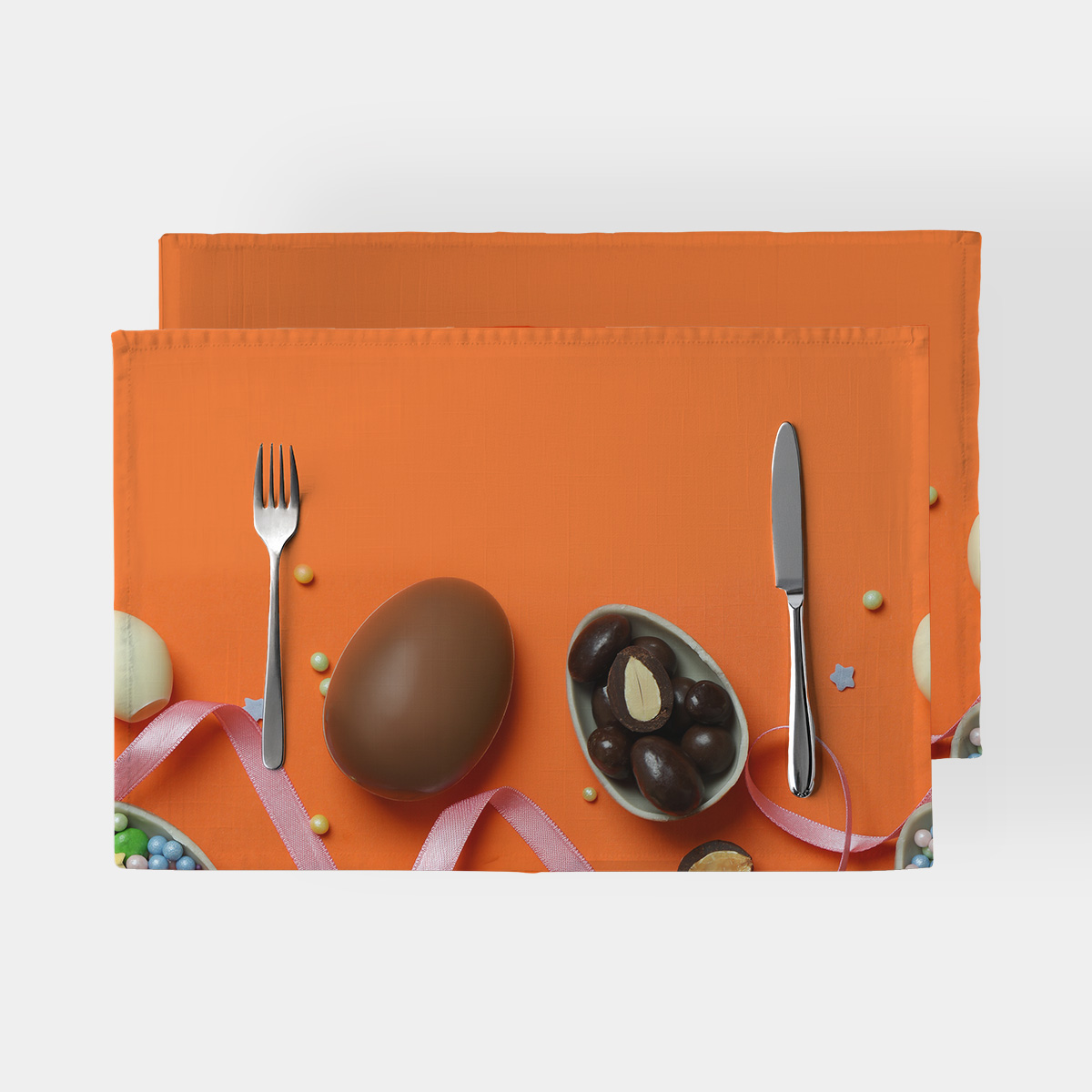 Podkładka z motywem kakaowej pisanki i różową wstążką na intensywnym pomarańczowym tle, ujęcie od góry