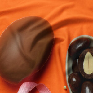 Zbliżenie na czekoladową pisankę i miseczkę z drażami na pomarańczowej tkaninie