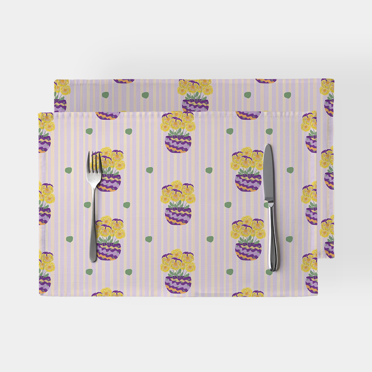 Dwie podkładki na stole z motywem pastelowych pasów i doniczek z żółtymi bratkami ułożone obok sztućców