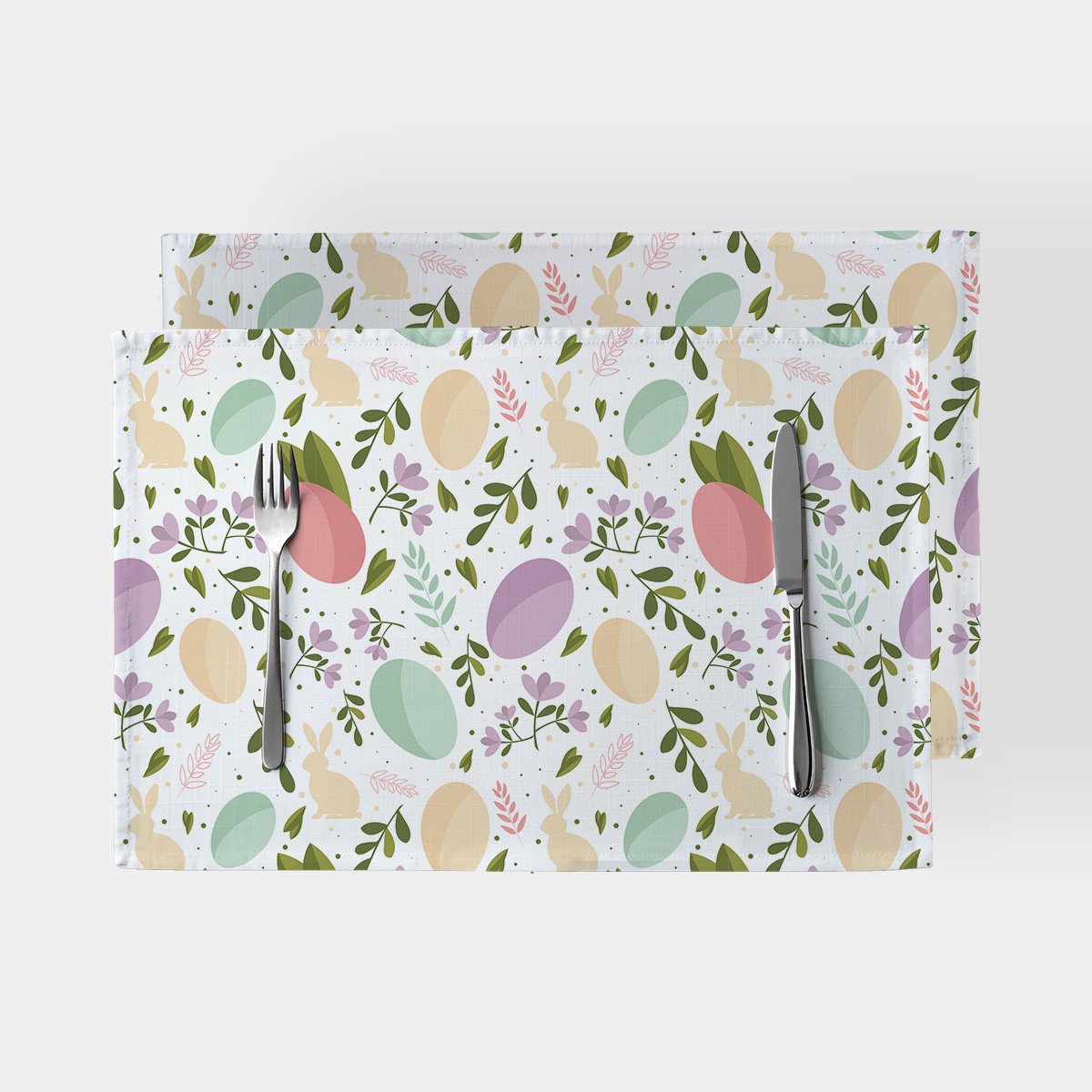 Dwie podkładki z motywem pastelowych pisanek i zajączków, widok z góry ze sztućcami