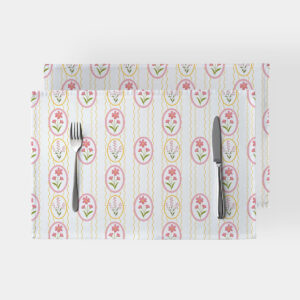 Dwie podkładki na stół z pastelowym wzorem pisanek i różowych kwiatów ułożone jedna na drugiej z widocznymi sztućcami