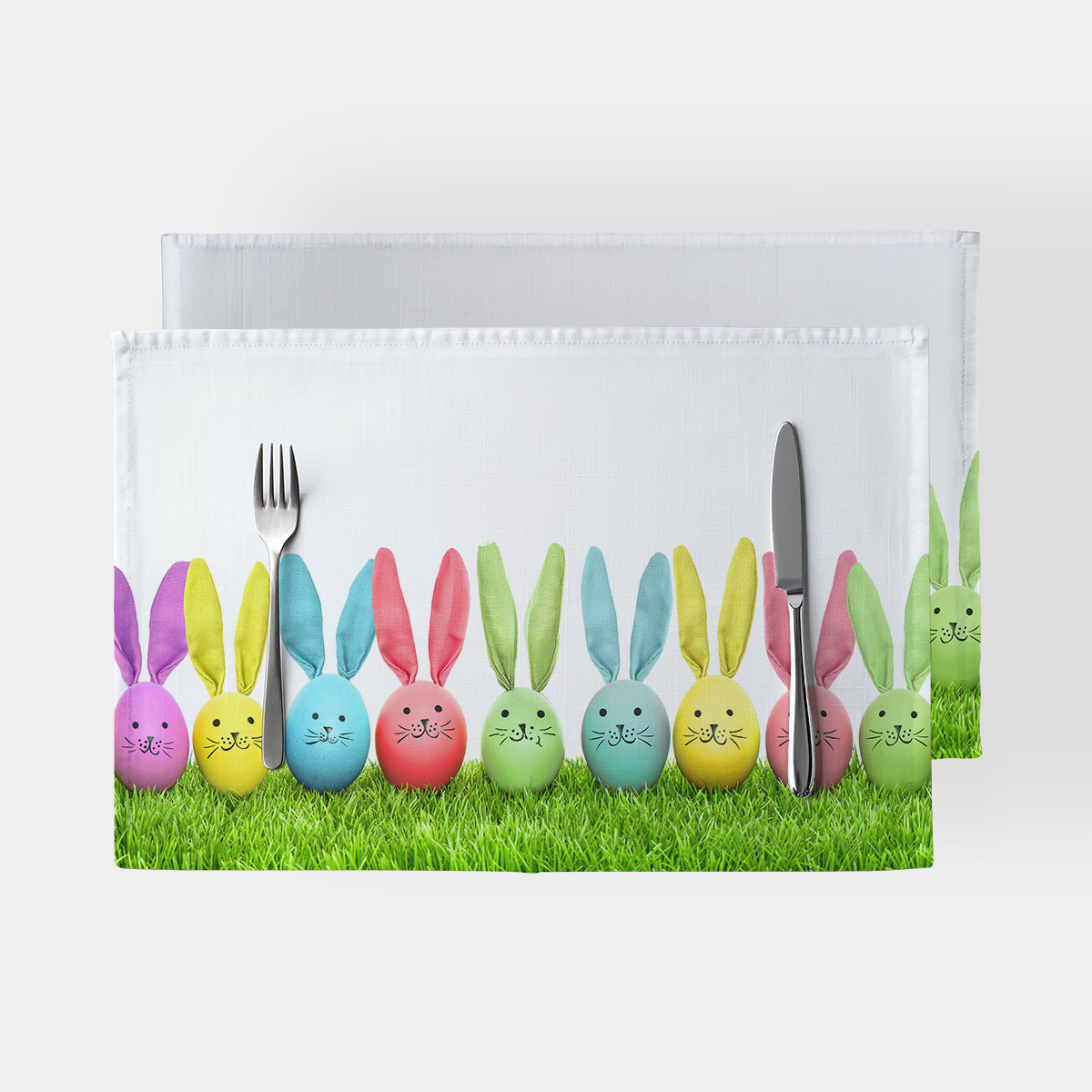 Główne ujęcie podkładki z rzędem pastelowych jajek z uszami króliczka na zielonej trawie z widocznymi sztućcami