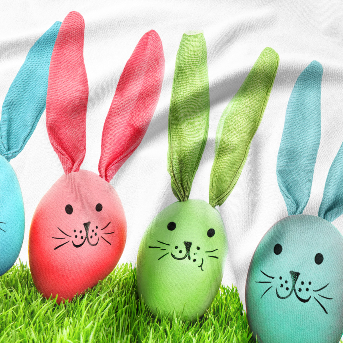 Zbliżenie na detal tkaniny, uszy króliczków i rysowane twarzyki na kolorowych pisankach