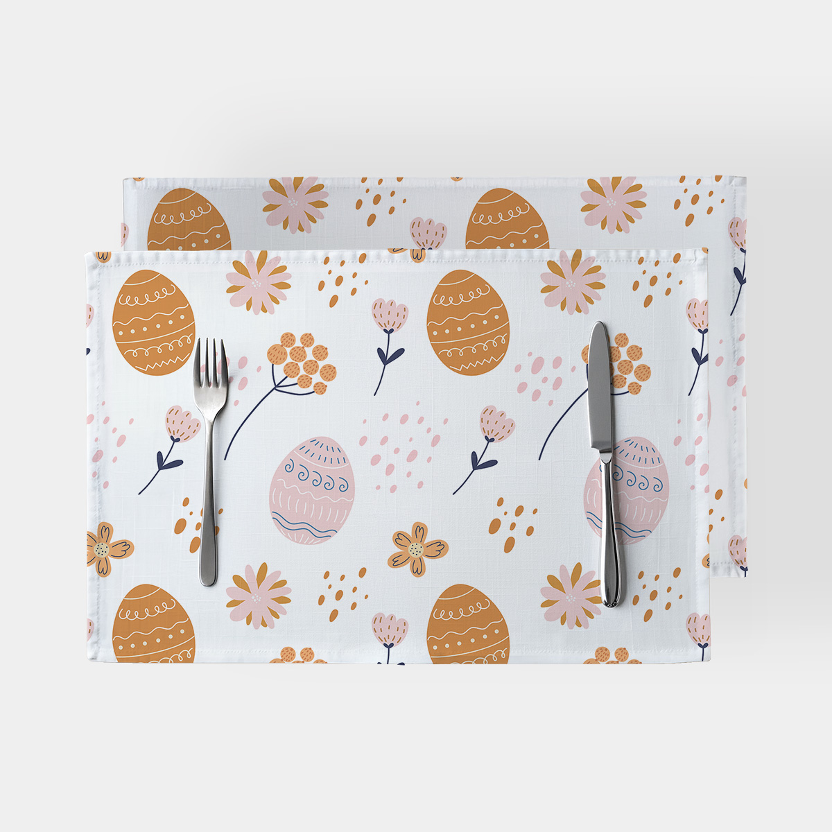 Para podkładek przedstawiona na białym tle z wzorem pisanek i drobnych kwiatów oraz widocznymi sztućcami