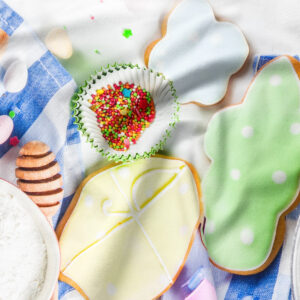 Zbliżenie na lukrowane ciasteczka, kolorowe posypki i przybory do pieczenia na tkaninie