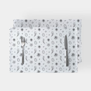Para białych podkładek z czarno-białym wzorem pisanek i kwiatów na jasnym tle z widocznymi sztućcami