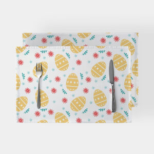 Dwie podkładki z motywem żółtych pisanek i drobnych czerwonych oraz błękitnych kwiatów ułożone na jasnym tle ze sztućcami