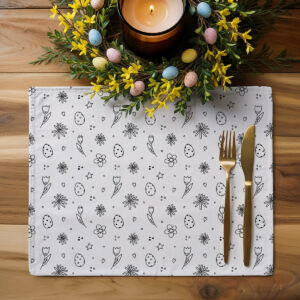 Podkładka na drewnianym blacie obok złotych sztućców i wiosennego stroika z kolorowymi pisankami