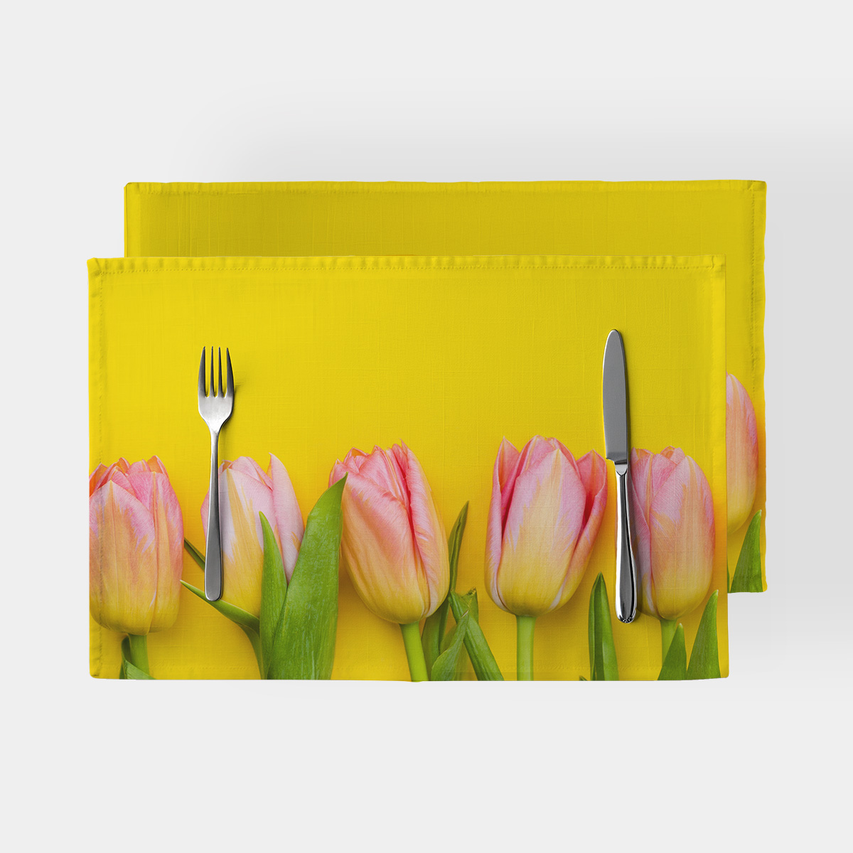 Podkładka z różowymi tulipanami na żółtym tle, ujęcie z góry z widocznymi sztućcami