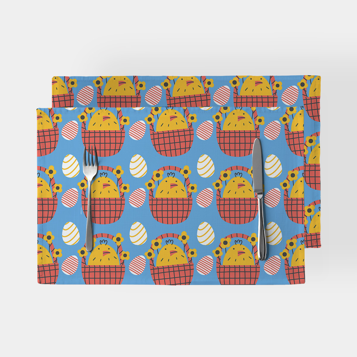 Dwie podkładki na stół z wzorem wielkanocnych kurczaczków w czerwonych koszykach na niebieskim tle