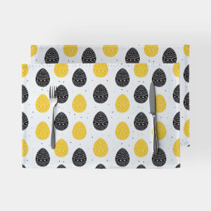 para podkładek na białym tle z wzorem żółtych i czarnych pisanek, widok z góry z nożem i widelcem
