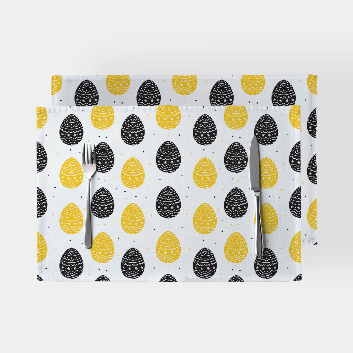 para podkładek na białym tle z wzorem żółtych i czarnych pisanek, widok z góry z nożem i widelcem