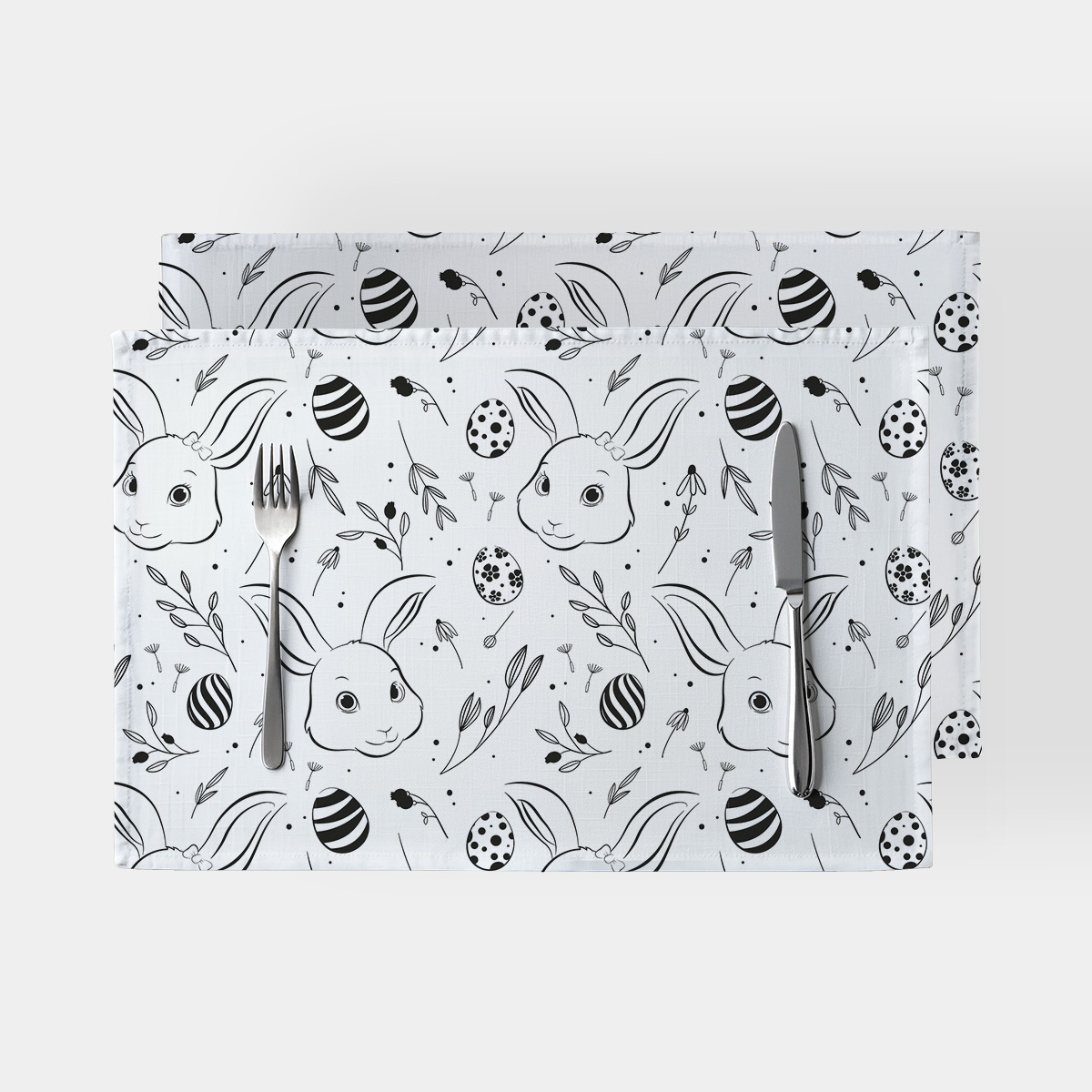 Para podkładek na stół z wzorem króliczków i pisanek, ujęcie z góry z widocznymi sztućcami