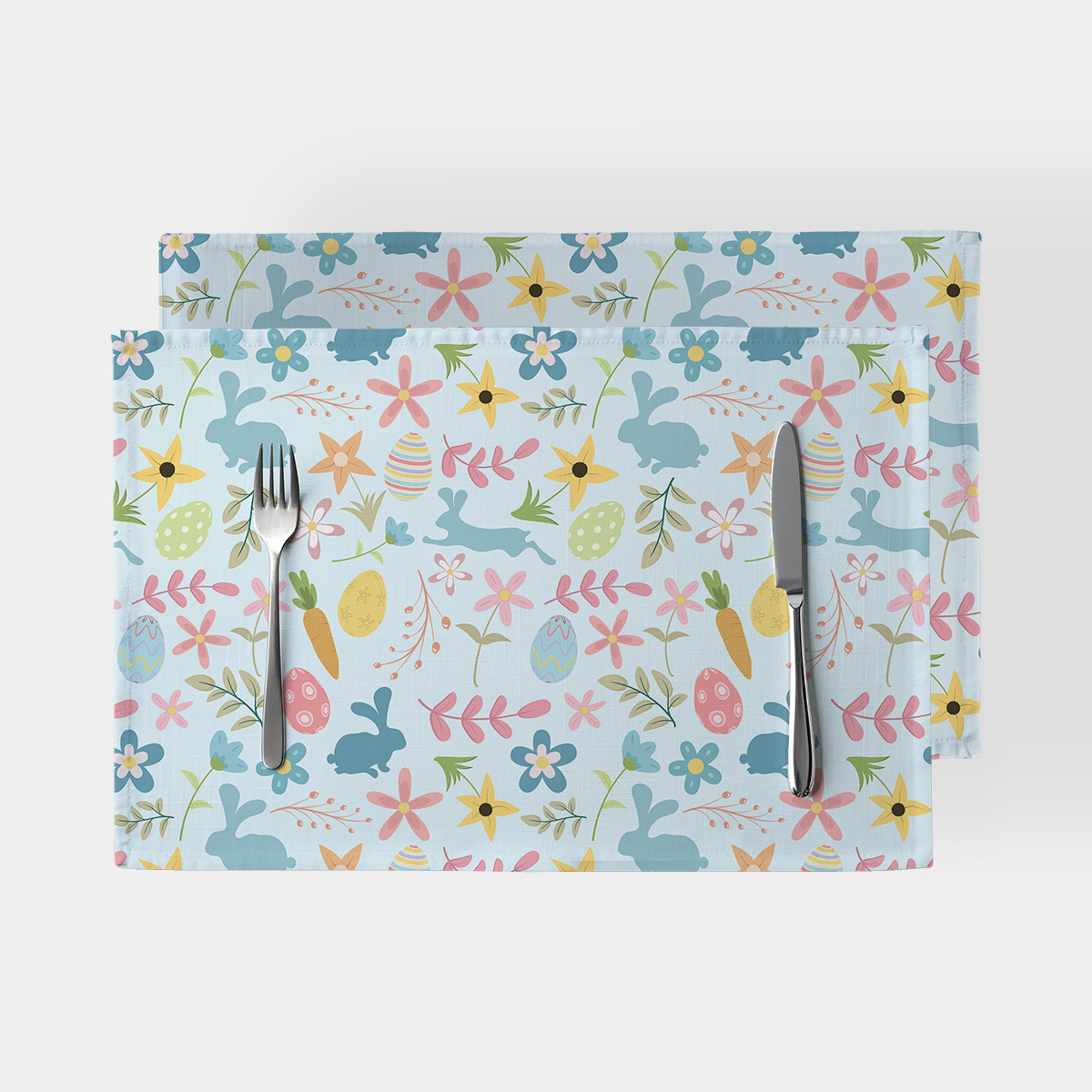 Dwie podkładki na stole z pastelowym wzorem zajączków, pisanek i kwiatów widziane z góry