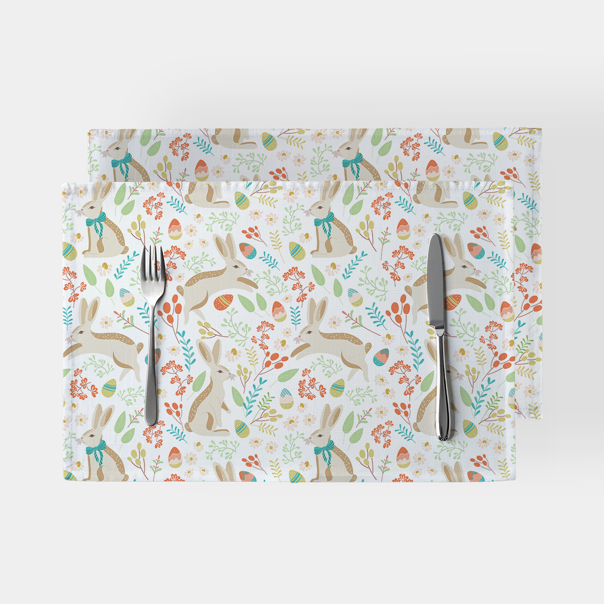 Dwie podkładki z motywem zajączków i pisanek ułożone jedna na drugiej z widocznym widelcem i nożem
