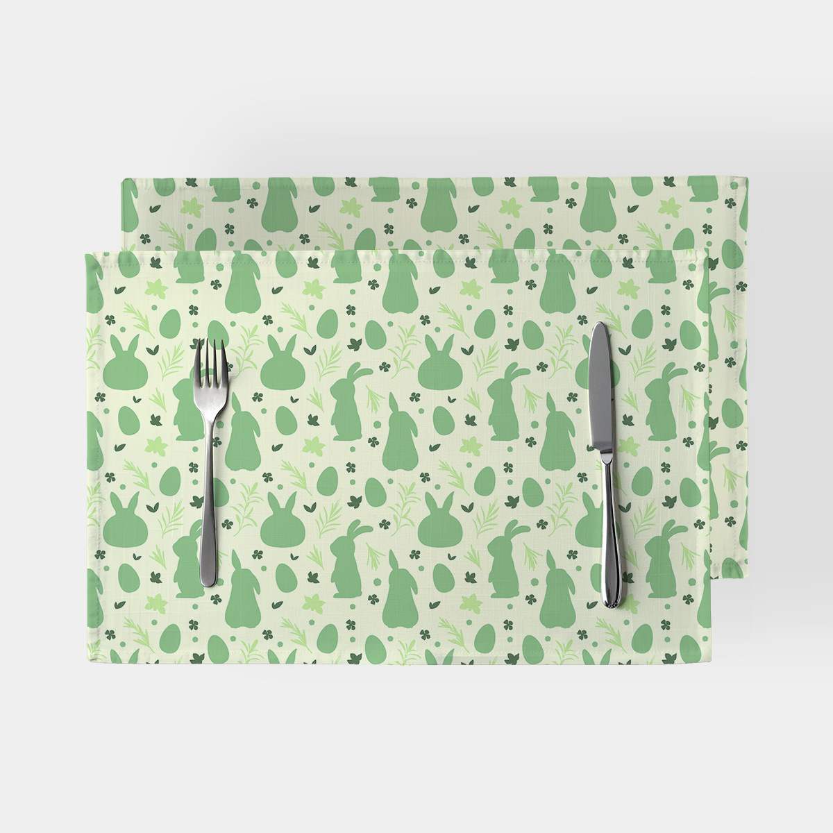 Dwie podkładki na stole z zielonym wzorem zajączków i sztućcami ułożonymi na jednej z nich