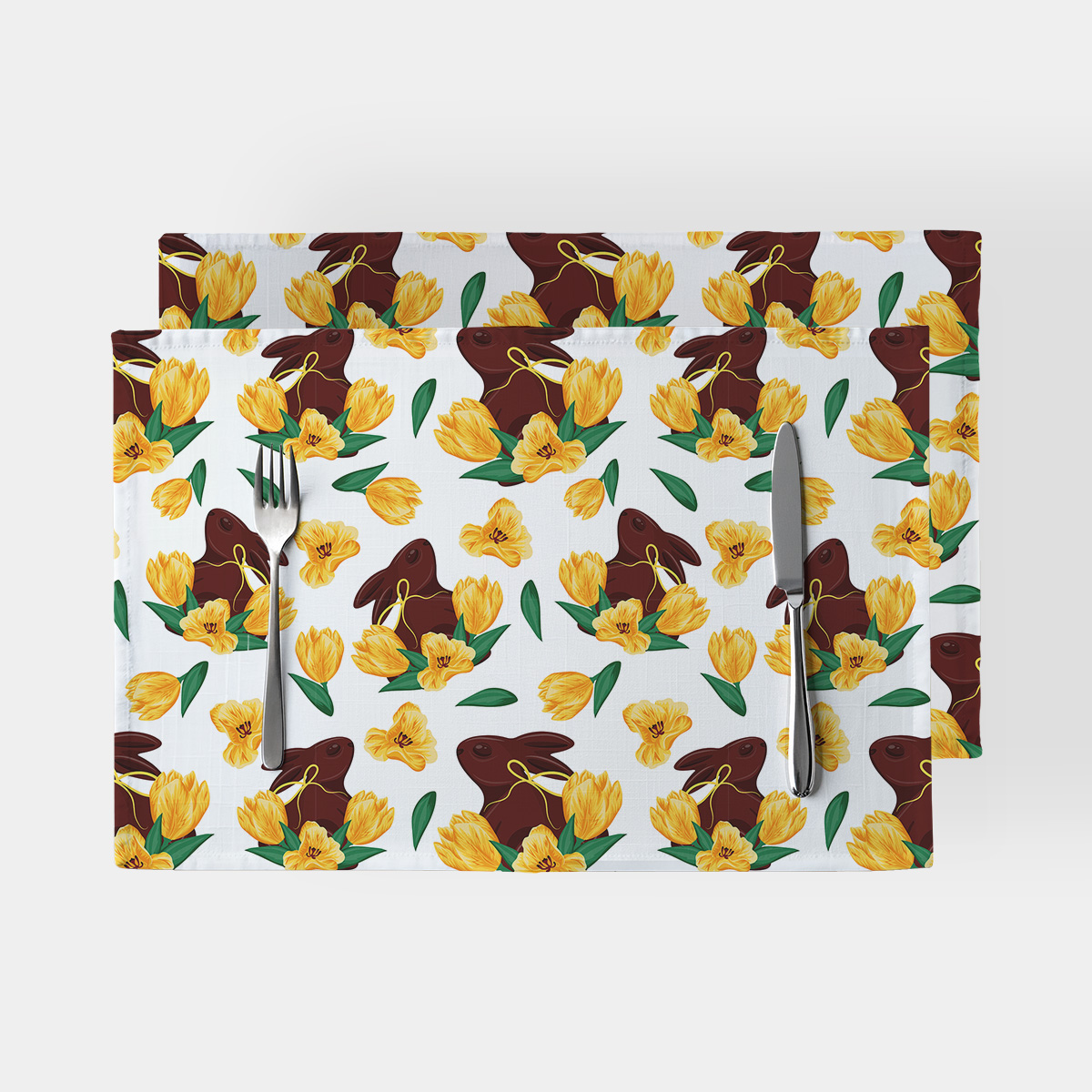 Podkładki na stół z wzorem czekoladowych zajączków i żółtych tulipanów na białym tle, ujęcie od góry