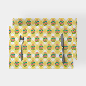Dwie podkładki w żółtą kratę z kolorowymi pisankami ułożone na stole z nożem i widelcem, widok z góry