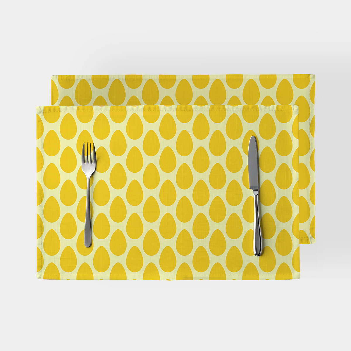 Dwie podkładki na stół z wzorem żółtych pisanek, ustawione jedna na drugiej z nożem i widelcem