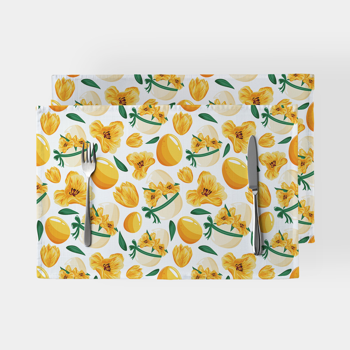 Dwie podkładki na stół z motywem żółtych pisanek i wiosennych kwiatów na białym tle ze sztućcami