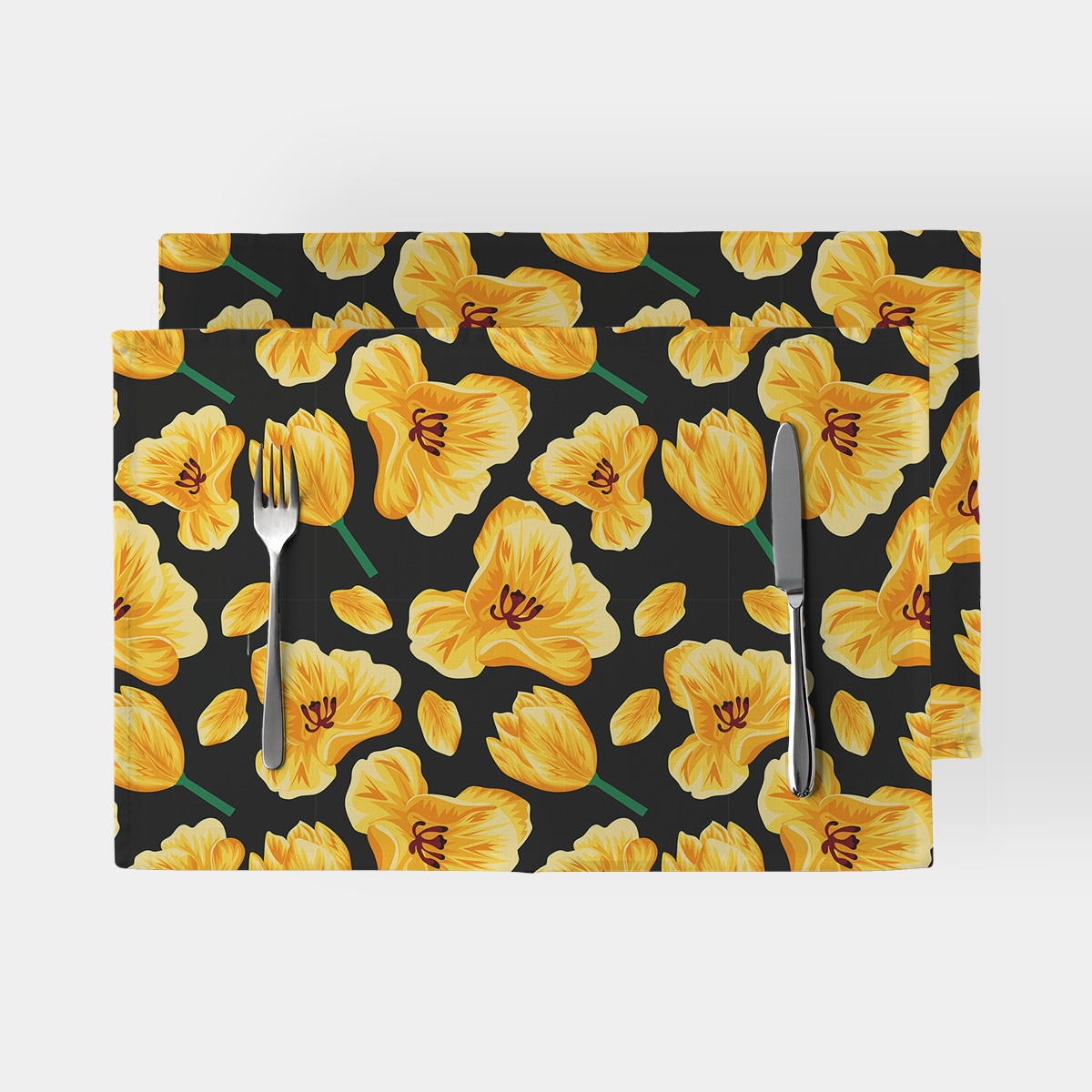 Dwie podkładki z wzorem żółtych tulipanów na czarnym tle ułożone jedna na drugiej z sztućcami
