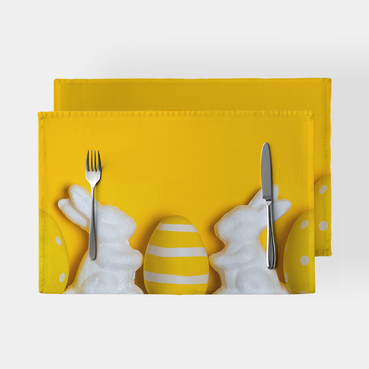 Żółta podkładka z białymi króliczkami i pasiastym jajkiem widziana z góry