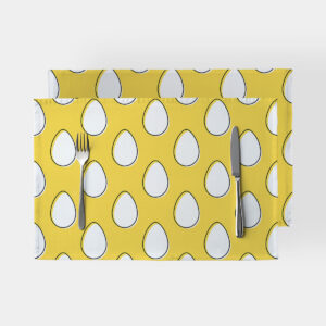 Dwie żółte podkładki na stół z powtarzającym się wzorem białych pisanek, widok z góry ze sztućcami