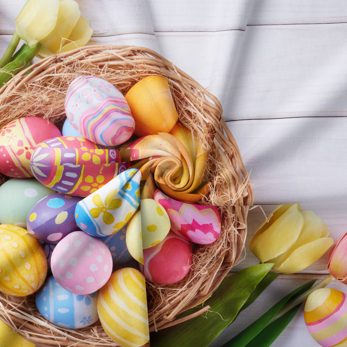 zbliżenie na koszyk z barwnymi pisankami i detal tkaniny obrusa