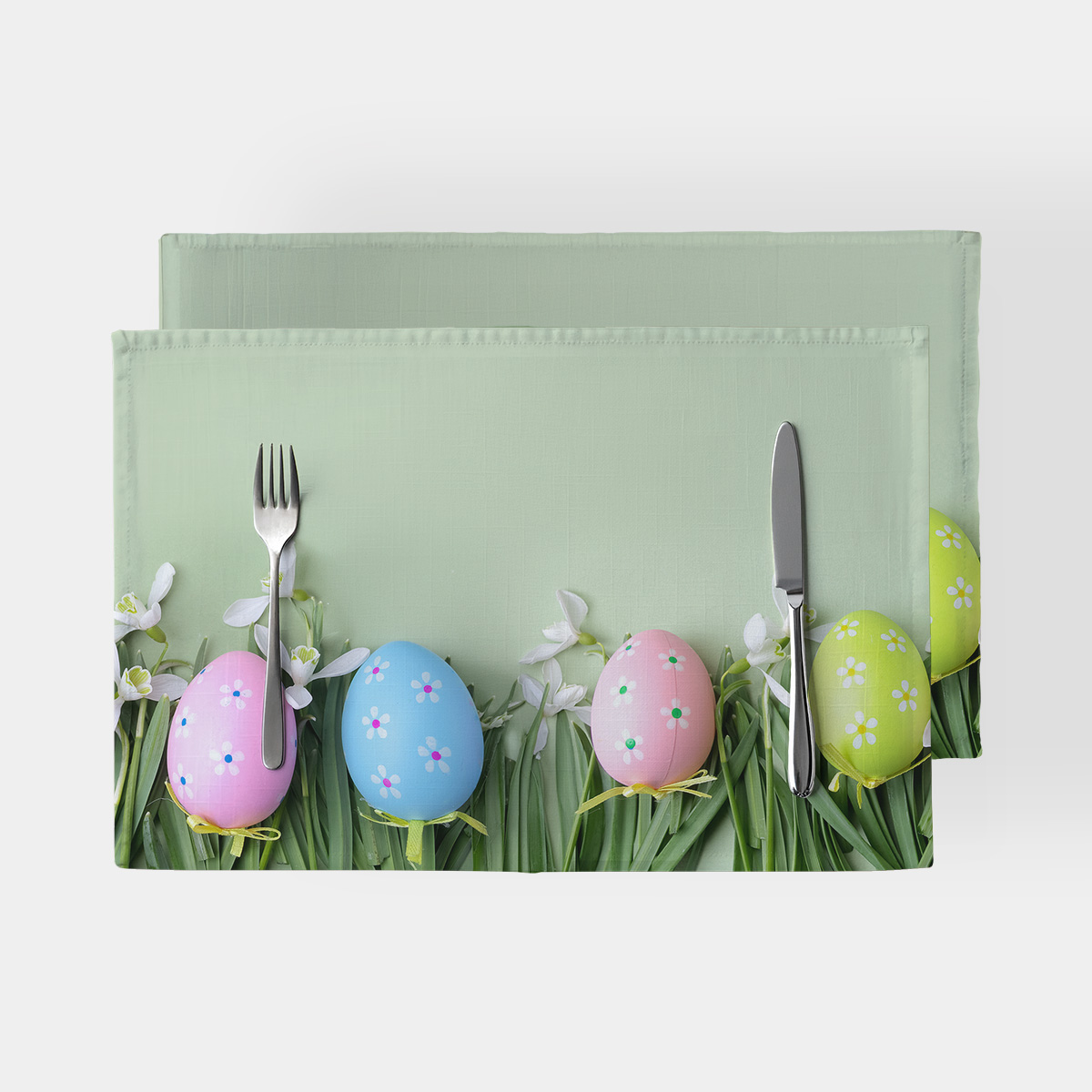 podkładka z motywem pastelowych pisanek na zielonym trawniku z ustawionymi sztućcami