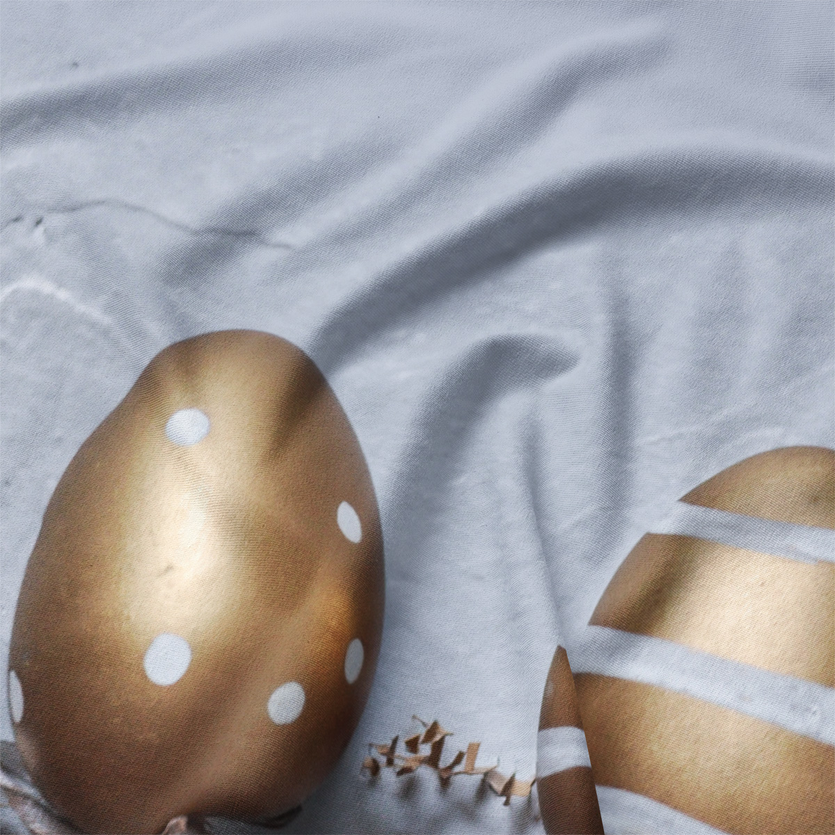 Zbliżenie na złotą pisankę z białymi kropkami i fakturę tkaniny