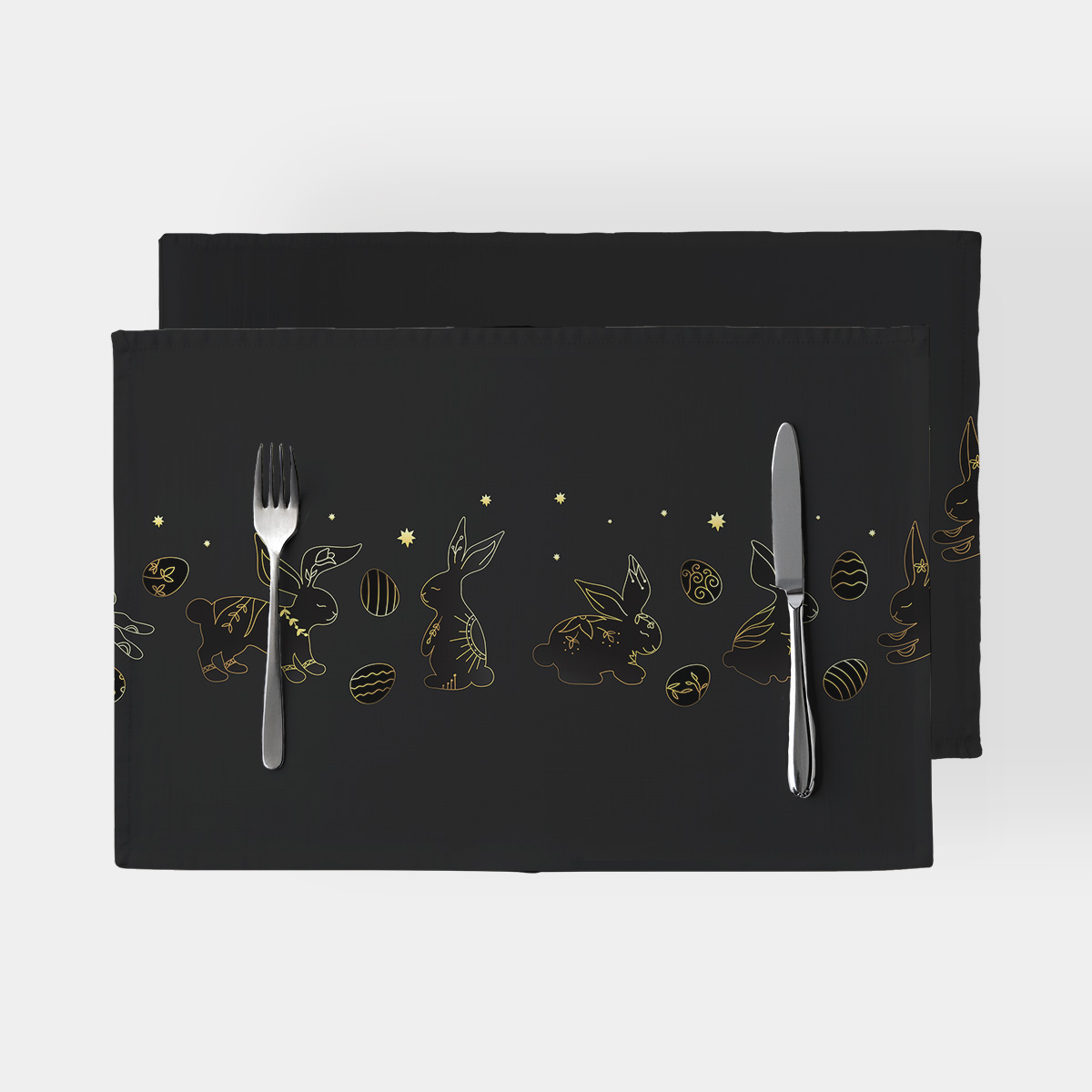 Czarne podkładki z rzędem złotych konturowych zajączków i pisanek ułożone na stole ze sztućcami