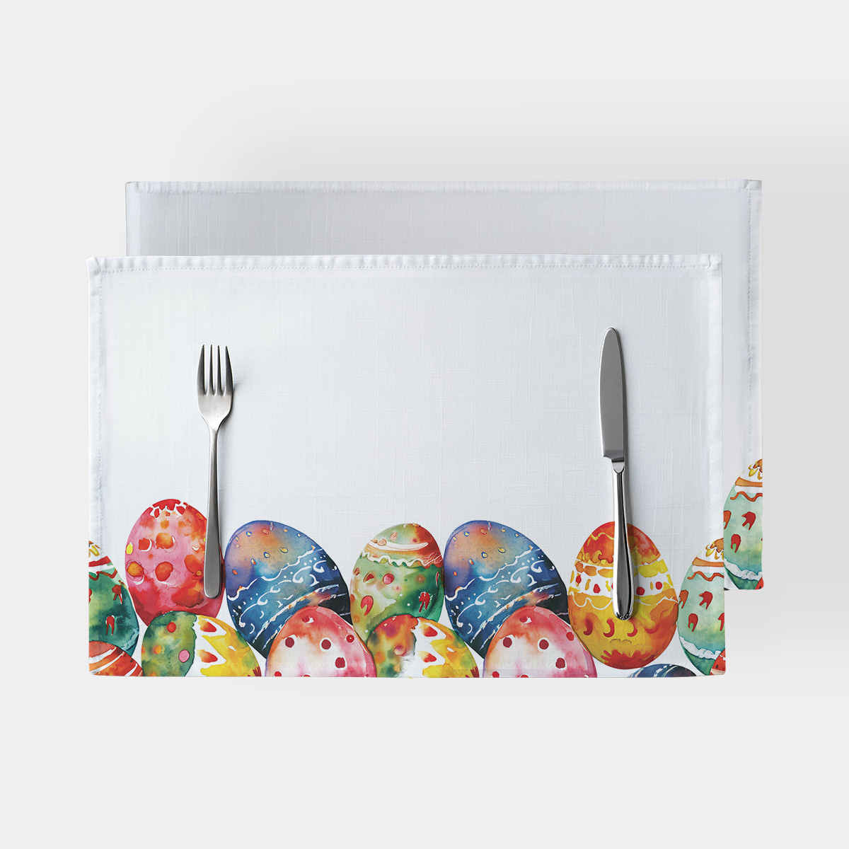 biała podkładka z akwarelowymi pisankami przy dolnej krawędzi, widok z góry z nożem i widelcem