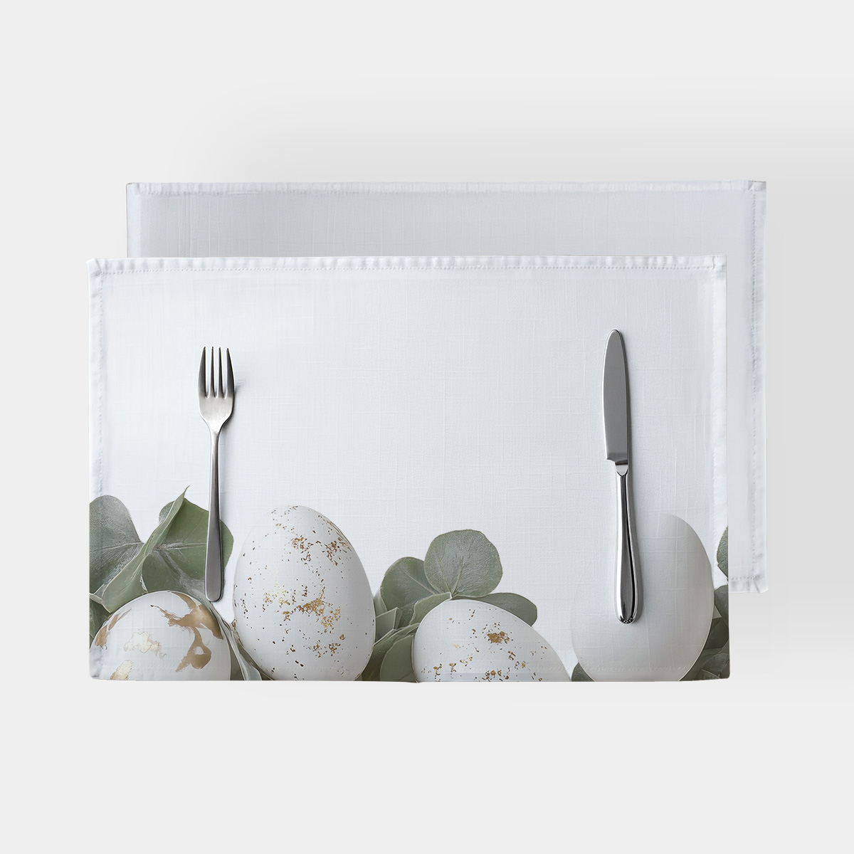 Główne ujęcie białych podkładek z motywem pisanek ze złotymi plamkami i liśćmi eukaliptusa