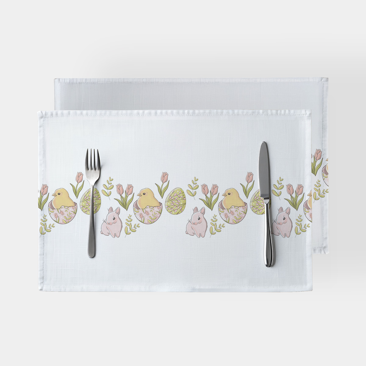 Dwie podkładki z nadrukiem kurczaczków, pisanek i gałązek na białym tle ułożone jedna na drugiej