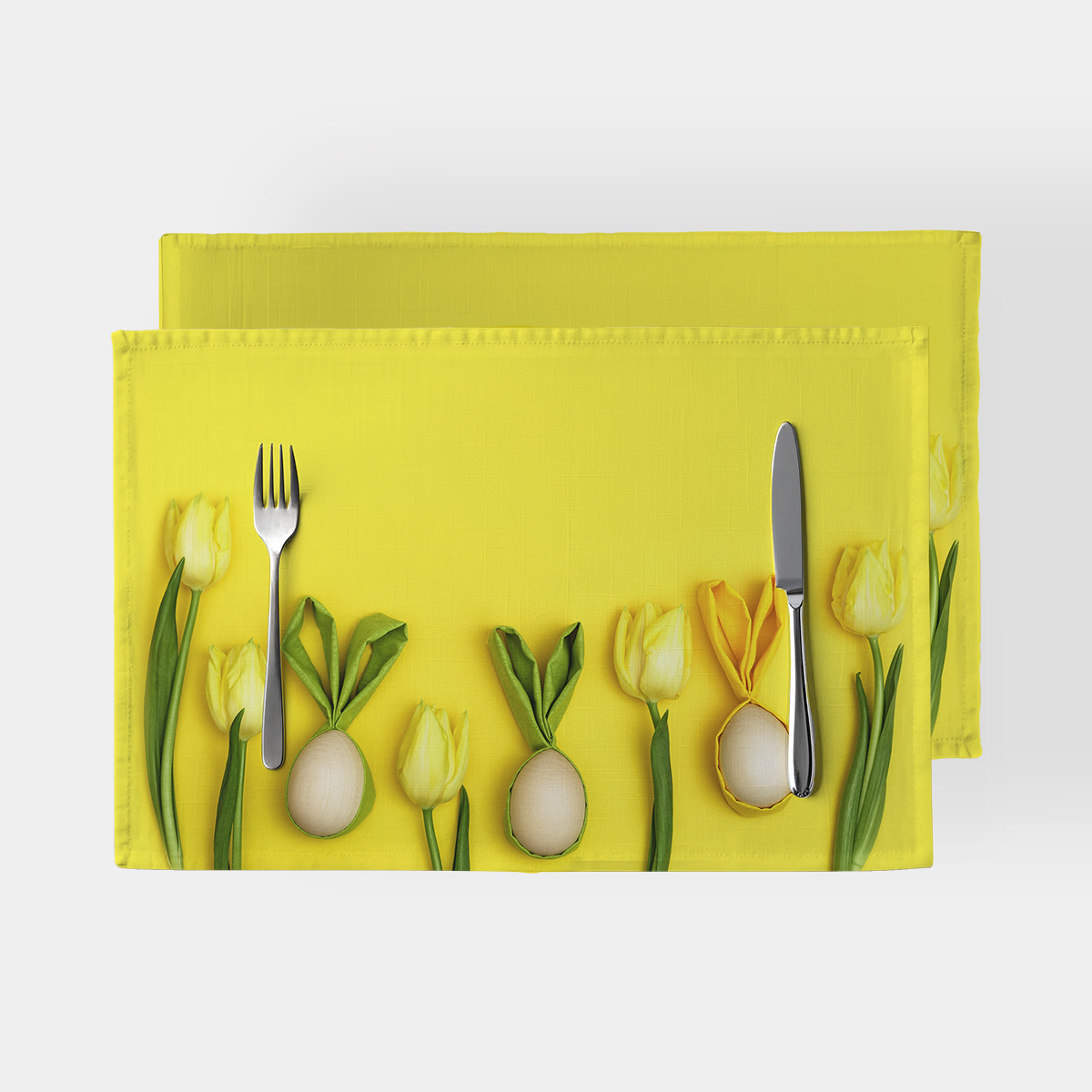 Żółta prostokątna podkładka z tulipanami i ozdobnymi pisankami w centralnym ujęciu pod talerzem i sztućcami