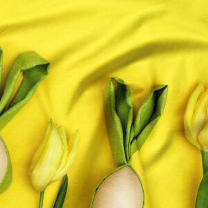 Zbliżenie na detal tkaniny: zielone liście tulipanów i brzegi pisanek na intensywnie żółtym tle