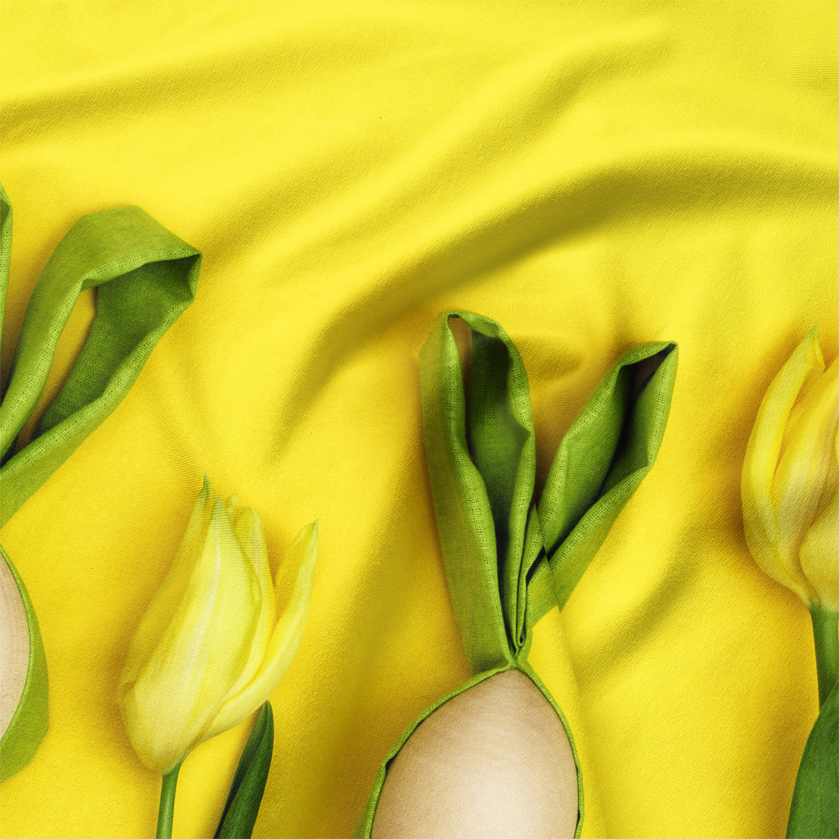 Zbliżenie na detal tkaniny: zielone liście tulipanów i brzegi pisanek na intensywnie żółtym tle