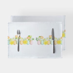 biała podkładka z poziomym paskiem pastelowych jajek i żółtych kwiatów, ujęcie z góry z widocznymi sztućcami