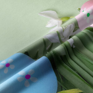 Zbliżenie na fakturę tkaniny i detal pisanek z drobnymi kwiatkami oraz zielonymi źdźbłami trawy