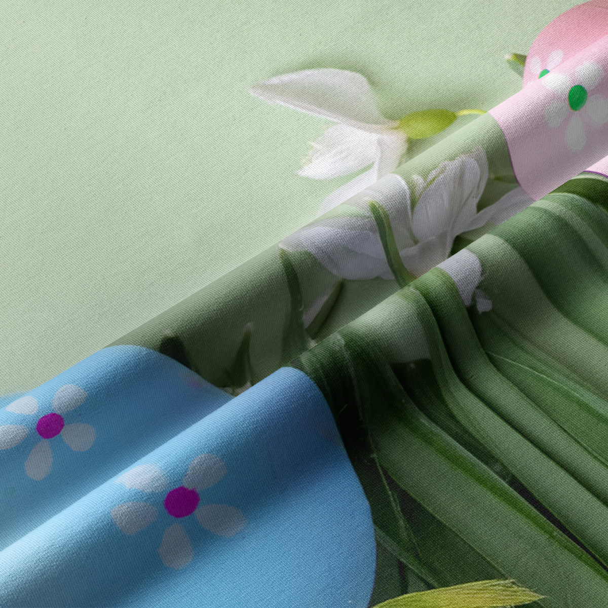 Zbliżenie na fakturę tkaniny i detal pisanek z drobnymi kwiatkami oraz zielonymi źdźbłami trawy